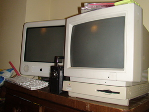 A Macintosh Peforma 450 with the newer style case design displayed on a clothing drawer with the Performa Plus displayed paired on top of it. An eMac is also visible to the left of the Performa, along with a Roberts boombox peeking out as well. There's also two random CDs and a green audio cassette sitting on top of the Performa Plus display... for some reason