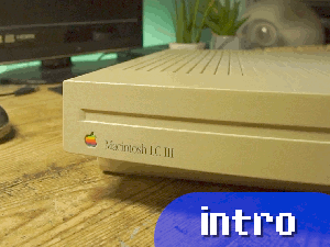 Link to the intro segement of this video. The thumbnail is a closeup of the front case of the LC III, showing the rainbow Apple logo and Garamound font branding on the left side. The computer is placed on a desk which has an LED strip light behind it set to green. Other items visible include a 15 inch 720p TV on the left and an iMac G4 to the right. A blue rounded button is added to the thumbnail, which says "intro" in a pixel style font