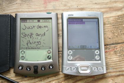 Palm Vx and Tungsten E2 both shown together. The Vx is displaying a handwritten note saying 'Just doing stuff and things', with the word 'things' being circled. The E2 is displaying text in Courier New that reads 'Hello world!!'