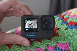 Front of the GoPro Hero 10 Black. In the photo, the camera is turned on and displaying the live preview on the front LCD, along with record time, battery percentage and video resolution (which was at 4K 50fps in the Linear FOV in this case). The live preview shows me as I was taking this photo from a slightly low angle, smiling towards the GoPro camera.