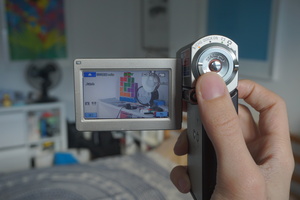 Sony HDR-TG3 Camcorder turned on in the main camera mode; zoomed in to a Tetris light, speech bubble whiteboard and other things on top of a low shelf