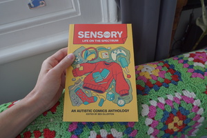 The physical copy for Sensory: Life on the Spectrum being held up in my hand towards the camera, showing the front cover
