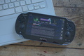 Photo of an original Playstation Vita (PCH-1000) displaying an earlier version of the index page, using the built-in web browser. The Vita itself is placed on the corner of a Mid 2009 polycarbonate MacBook, which was locally hosting the page