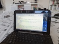 Photo of a Compaq Mini netbook displaying a work in progress version of the about page on this site, under the Geany text editor in antiX Linux. In particular, I took this before writing the "facts about me" section, so the page only had the image and basic bio